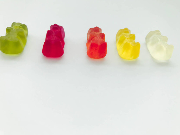 gummy bears of bright, different colors on a blue matte background. delicious mouth-watering candies of an unusual shape. high-calorie dessert. calories for weight gain, sugar sweetness - Foto, afbeelding