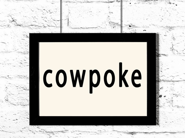 Cadre noir accroché au mur de briques blanches avec inscription cowpoke - Photo, image