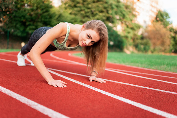 Athletic girl stands in the plank at the stadium runway - Foto, Imagem