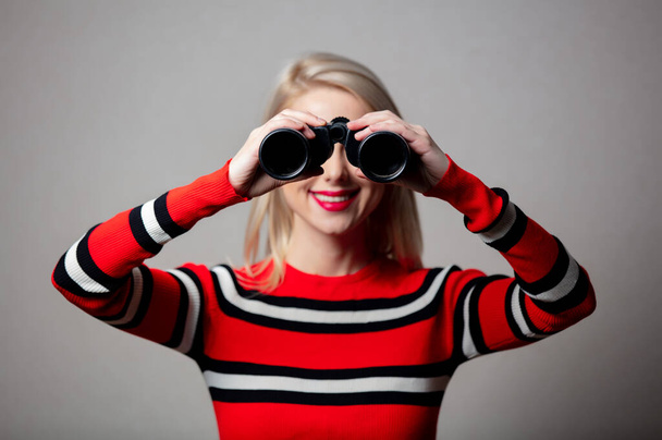 blonde in red sweater with binoculars on grey background  - Foto, Bild