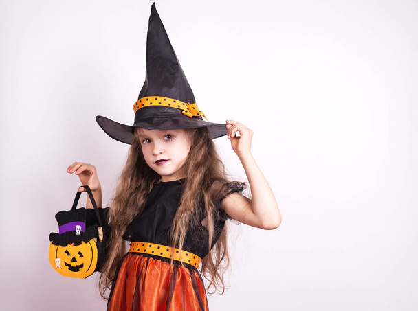 Счастливая маленькая смеющаяся девочка в костюме ведьмы на карнавале, играющая с корзиной за угощениями. Девочка Хэллоуин ребенок на белом фоне. - Фото, изображение