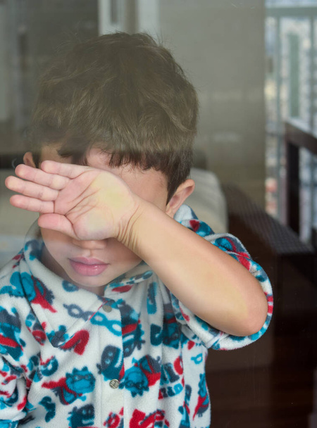 παιδί κρύβεται πρόσωπο με το χέρι πίσω από το γυαλί - Φωτογραφία, εικόνα