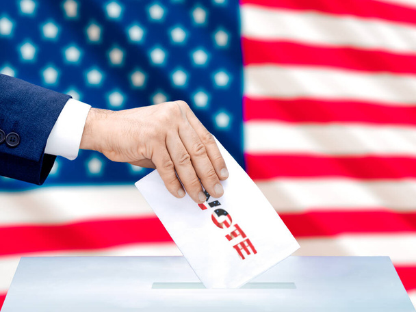 Une main d'homme votant à l'élection présidentielle américaine avec le drapeau américain derrière elle. Concentration sélective - Photo, image