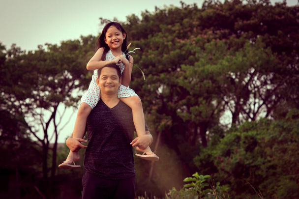 Asian little child girl riding on father's shoulders in the green natural background.Vintage color style - Photo, Image