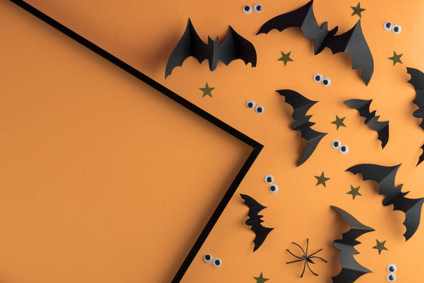 Modèle de cadre Halloween avec des chauves-souris en papier noir et des yeux effrayants en plastique sur un fond jaune coloré. - Photo, image