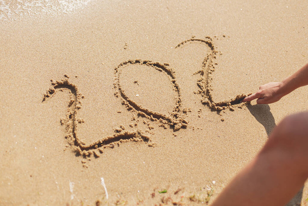 Persona escribiendo 2021 signo en la playa de arena, dos y cero inscripción primer plano. Feliz año nuevo 2021 o 2022 y vacaciones de verano! Bienvenida 2021 con nuevas resoluciones, sueños, listas - Foto, imagen