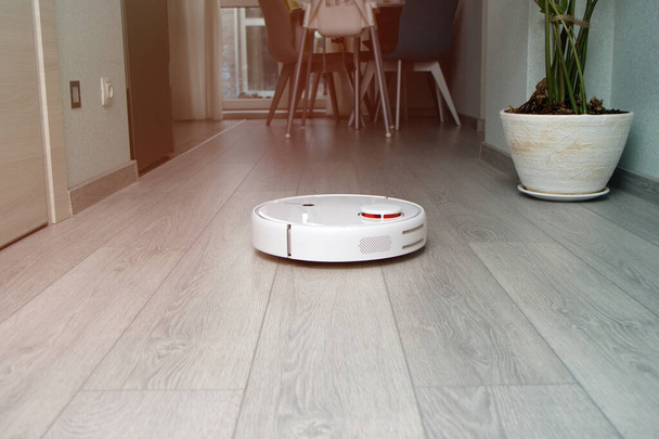 robot vacuum cleaner cleans the apartment. white robot vacuum cleaner work in interior - Zdjęcie, obraz