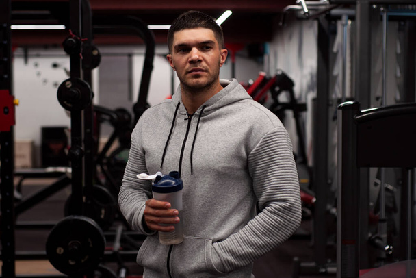 Muscular men drinks protein or water, energy drink in the gym. Sportsman holding a shaker - Fotografie, Obrázek