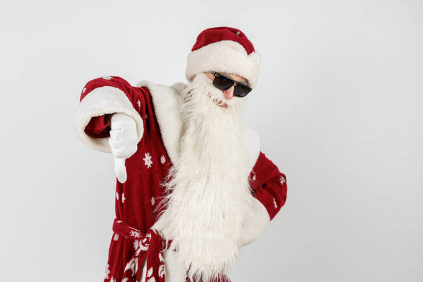 Concepto de Navidad y Año Nuevo. Santa Claus muestra un gesto de mano con el dedo hacia abajo. Fondo aislado. - Foto, Imagen
