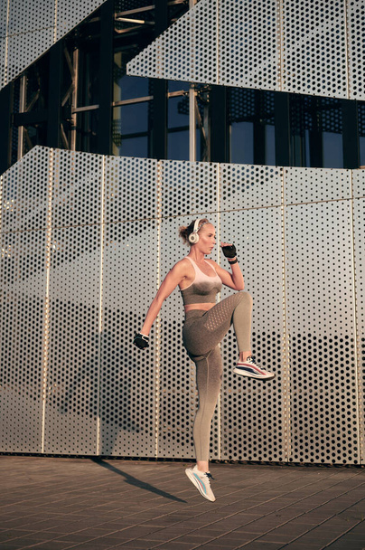 Erős nő, aki a szabadban edz, és fejhallgatóba ugrik a fal előtt. Egészséges fiatal női sportoló fitness edzés és zenehallgatás - Fotó, kép
