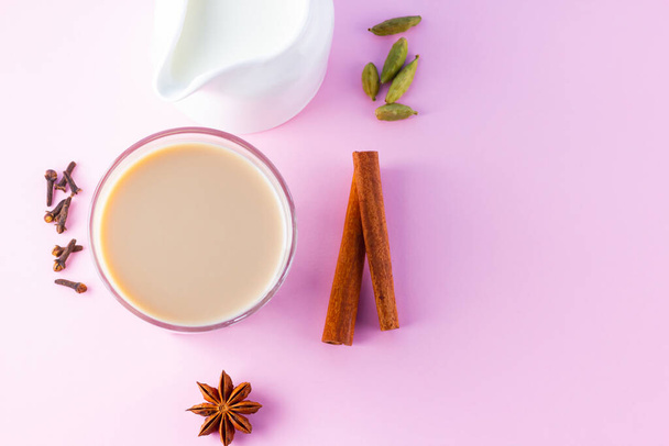 Masala tea and spices on a pink background. Masala chai in glass. Indian national drink and milk jug on a pastel background. Copy space. Top view - Photo, Image