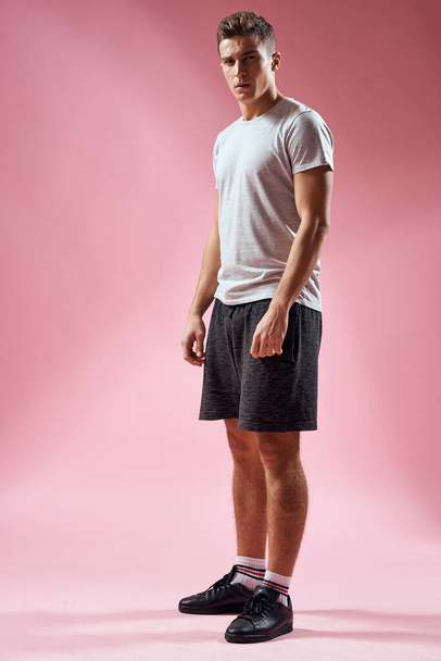 Un hombre en pantalones cortos deportivos en una camiseta y zapatillas de deporte sobre un fondo rosa en pleno crecimiento - Foto, Imagen