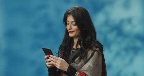 Młoda, ładna Hinduska kobieta w tradycyjnym stroju podsłuchuje i pisze smsy przez telefon komórkowy i uśmiecha się. Atrakcyjna Indianka przewijająca się przez komórkę. Dziewczyna na czacie z wiadomościami przez telefon. - Materiał filmowy, wideo