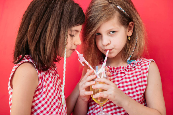 Two little girls drinking fruit juices from one single glass, sharing. - Foto, Bild