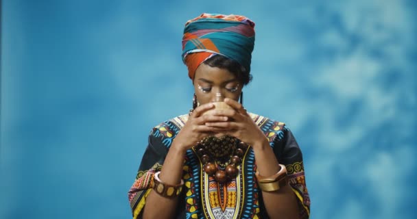 Αφρικανική αμερικανική νεαρή όμορφη γυναίκα σε παραδοσιακά ρούχα πίνοντας ζεστό τσάι και απολαμβάνοντας τη γεύση του. Όμορφη αναζητούν κομψό όμορφο κορίτσι από την Αφρική πίνοντας φυτικό ποτό από το κύπελλο. - Πλάνα, βίντεο