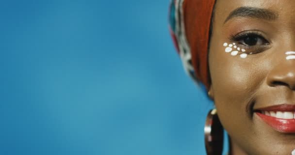Половина обличчя щасливої афро - американської вродливої дівчини з червоними губами радісно посміхаються до фотоапарата на синьому фоні стіни. Портрет красуні - Африки.. - Кадри, відео
