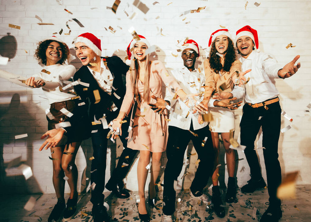 Чоловіки і жінки святкують Різдво стоячи під падінням Confetti в приміщенні
 - Фото, зображення