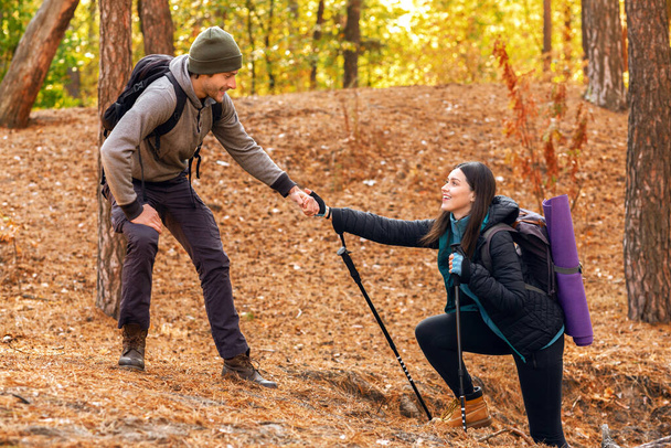 Caminante guapo ayudando a su novia cuesta arriba en el bosque - Foto, Imagen