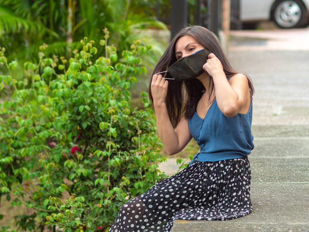 Jonge Latijns-Spaanse vrouw met een donkere handgemaakte gezicht masker zit op de stoep - Foto, afbeelding