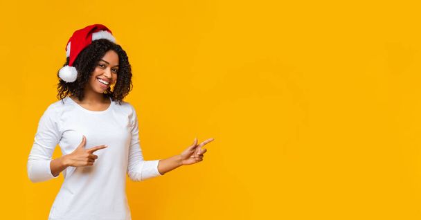 Black girl in santa hat pointing fingers aside at copy space - Foto, immagini