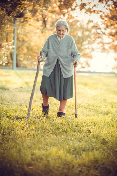 Starsza kobieta z laskami spacerująca w parku w pogodny jesienny dzień - Zdjęcie, obraz
