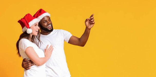 Happy interracial couple hugging and pointing with hand at copy space - Фото, зображення
