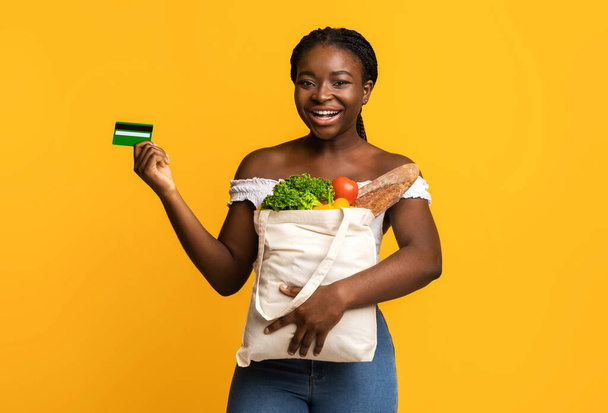 幸せな黒の女性を保持ショッピングバッグで食料品や示すクレジットカード - 写真・画像