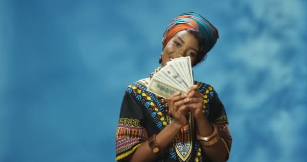 Πορτρέτο φωτογραφία της Αφρικής American νεαρή όμορφη γυναίκα με παραδοσιακά ρούχα μετρώντας τα χρήματα μπροστά από την κάμερα. Ελκυστική γυναίκα που κρατάει χαρτονομίσματα και δείχνει. Πλούσια κοριτσίστικη ιδέα. - Πλάνα, βίντεο