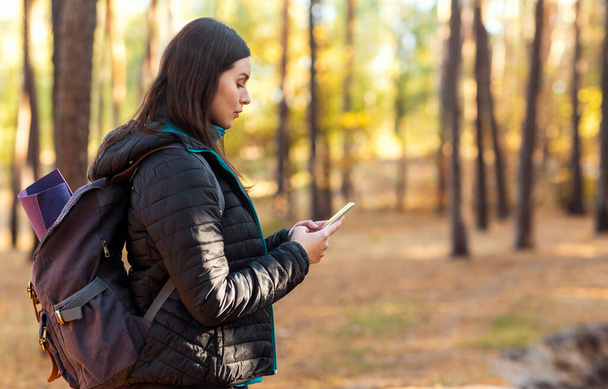 Poważna dziewczyna z plecakiem za pomocą telefonu komórkowego w lesie - Zdjęcie, obraz