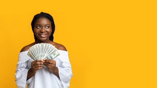 Pensive Bruneta žena drží peníze dolar v hotovosti a při pohledu na kopírovat prostor na žlutém pozadí, Přemýšlení o investičních plánech, Slavit finanční úspěch, Obdržený bonus, Panorama - Fotografie, Obrázek