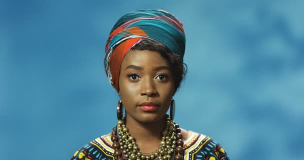 Portretfoto van mooie jonge Afro-Amerikaanse vrouw in traditionele kleding die er serieus uitziet voor de camera. Close-up van aantrekkelijke meisje kijken recht. Binnenshuis. Vrouwelijk gezicht. - Video