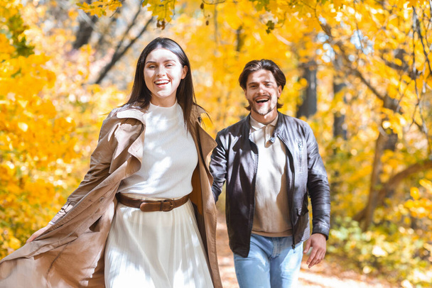Młody mężczyzna i kobieta biegnący przez jesienny las, trzymający się za ręce - Zdjęcie, obraz