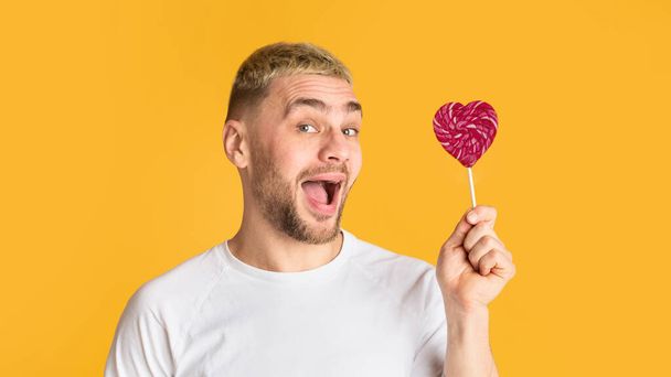 Emotional man with open mouth holds heart lollipop - Fotó, kép