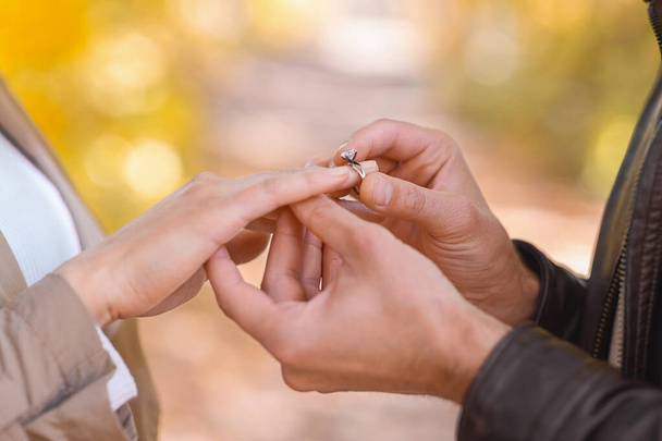 Mann legt Verlobungsring an Frauenhand im Freien - Foto, Bild