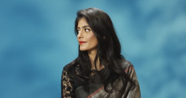 Portraitaufnahme von stilvollen Hindu junge attraktive fröhliche fröhliche Frau in traditionellem Look von Indien lächelt in die Kamera auf blauem Hintergrund. Nahaufnahme einer charmanten hübschen Frau mit Lächeln. - Filmmaterial, Video