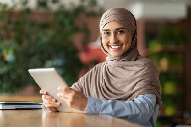 Kafede çalışan mutlu Arap kadın dijital tablet kullanıyor. - Fotoğraf, Görsel