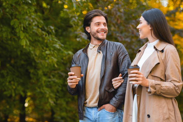 Cheerful man and woman drinking coffee while dating in forest - Foto, Imagem
