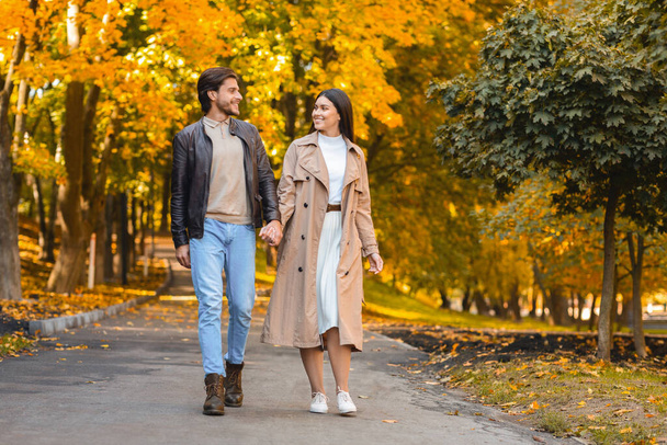 Positive man and woman holding hands and walking by park - Фото, изображение