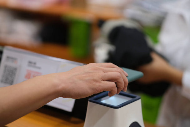 крупним планом рука тримає мобільний телефон для сканування, щоб платити в магазині одягу. м'який фокус
 - Фото, зображення