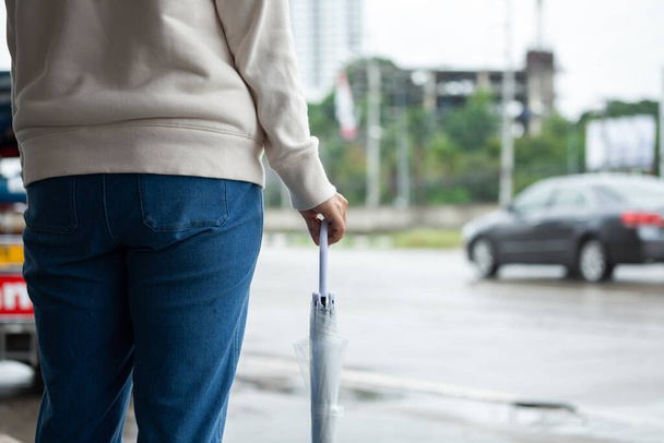 Aasian nainen tilalla sateenvarjo odottaessaan taksi ja seisoo kaupungin jalkakäytävällä kadulla sateisena päivänä. - Valokuva, kuva