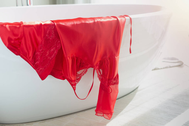 Luksusowa satynowa koszula nocna i szlafrok w czerwieni wiszące na wannie w łazience rano. - Zdjęcie, obraz