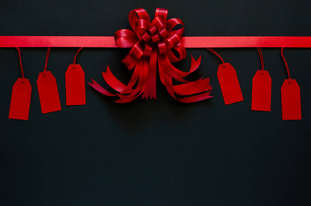 Red ribbon with bow and price tags on black background. Black friday concept. - Foto, imagen