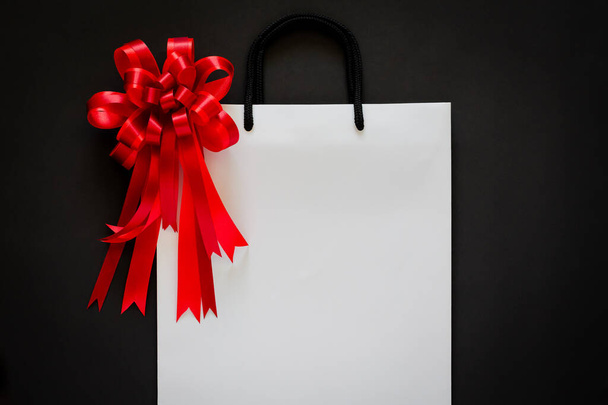 White shopping bag with red bow and ribbon on black background. Black friday concept. - Photo, Image