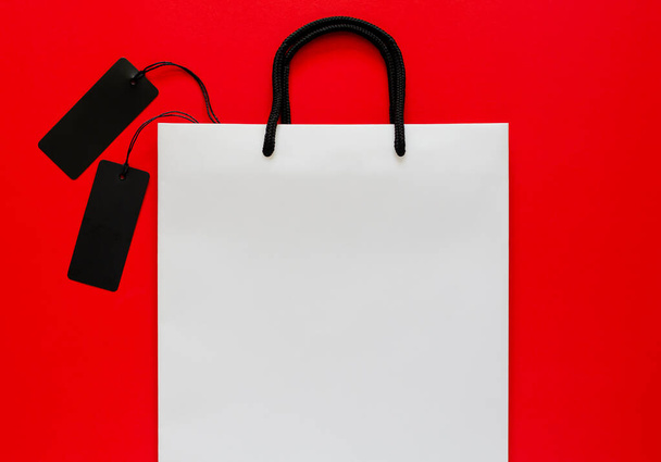 Weiße Einkaufstasche mit schwarzen Preisschildern auf rotem Hintergrund. Black-Friday-Konzept. - Foto, Bild