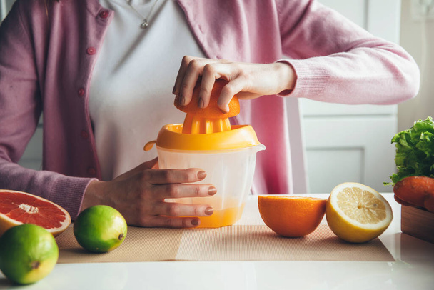 Közelkép egy nőről, aki gyümölcslevet készít otthon manuális facsaróval. - Fotó, kép