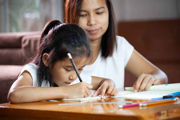 Jovem mãe asiática ajudando sua filha a fazer seu dever de casa em casa. Educação a partir de casa conceito. - Foto, Imagem