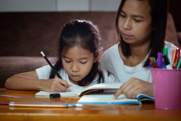 Giovane madre asiatica che aiuta la figlia a fare i compiti a casa. Istruzione dal concetto di casa. - Foto, immagini