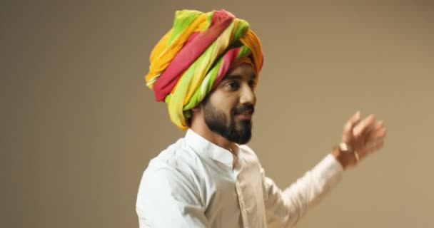 Close up of young Hindu handsome man in traditional colorful turban dancing and waving his hands. Male Indian cheerful dancer having fun and swaying with smile on face. - Footage, Video