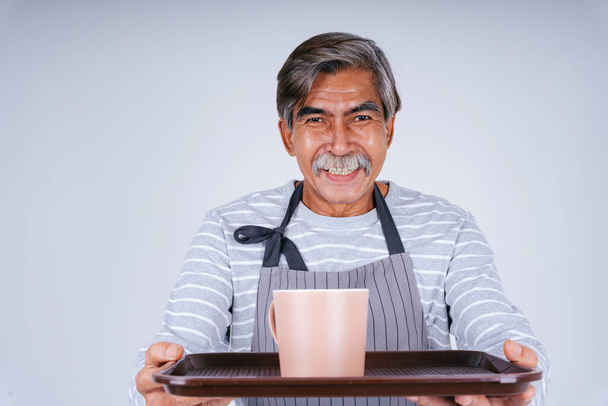 Портрет старого старшого офіціанта, який тримає чашку кави та лоток ізольовано на білому тлі
. - Фото, зображення