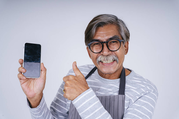 Портрет старого старшого офіціанта, який показує екран смартфона ізольовано на білому тлі
. - Фото, зображення